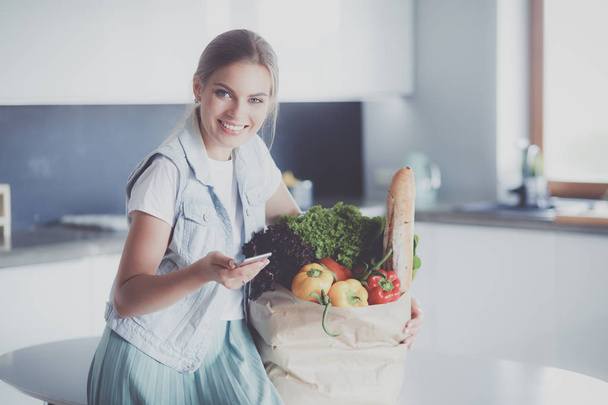 Young woman holding grocery shopping bag with vegetables .Standing in the kitchen - Zdjęcie, obraz