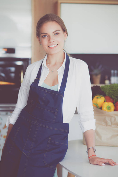 Portrait of young woman standing with arms crossed against kitchen background - Foto, afbeelding