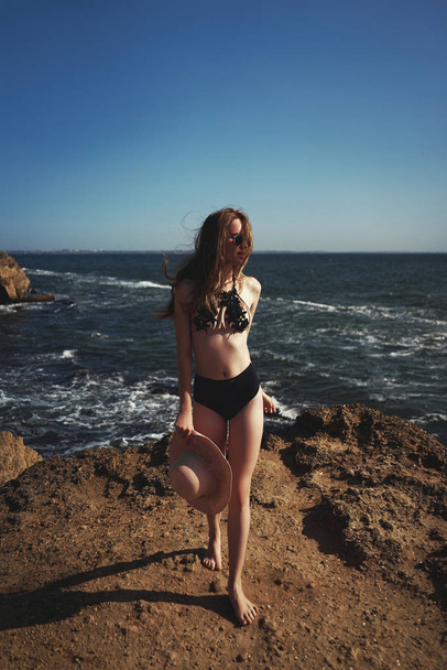 Girl enjoys relaxing near ocean. Concept travel, vacation. Model in swimsuit sunbathes on sand beach - Foto, imagen