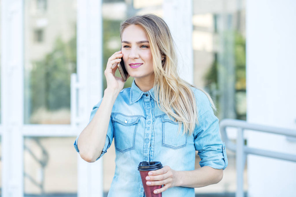 Jovem mulher em camisa jeans com smartphone. Conceito de estilo de vida, urbano, trabalho
 - Foto, Imagem