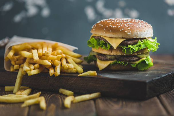 Burger con patate e birra scura su una tavola di legno su sfondo blu-grigio
 - Foto, immagini