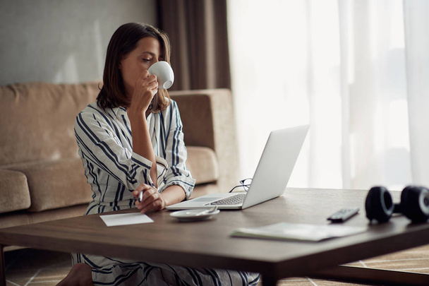young exhausted woman working at home with a laptop and drinking coffe - Foto, afbeelding
