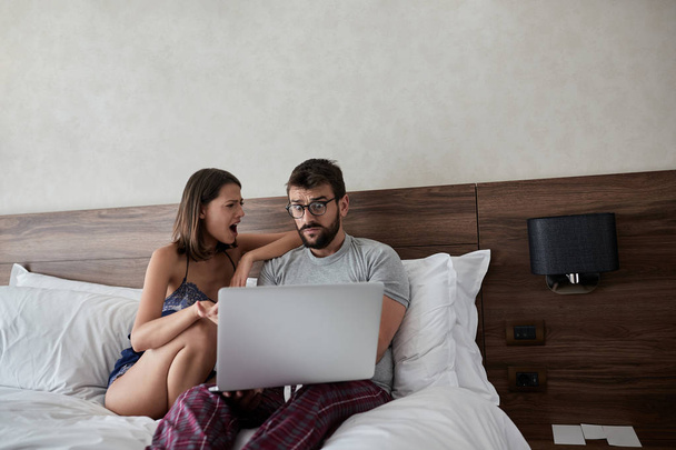 Young man and woman in the bed with laptop and surfing on internet. Modern lifestyle concept - Фото, зображення