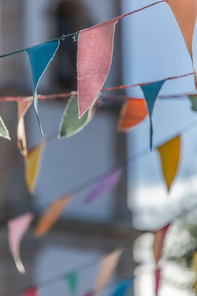 Ansicht der traditionellen Dekoration religiöser Feste auf den Dörfern, mit farbigen Papierdreiecken, die in Fäden hängen, Kirchturm im Hintergrund, in portugiesisch - Foto, Bild