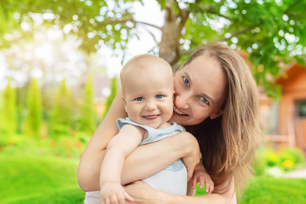 Beautiful mother with cute little baby boy having fun outdoors. Portrait of mom with fun child smiling in green summer garden. Happy family and parenting. Children care. - Photo, image