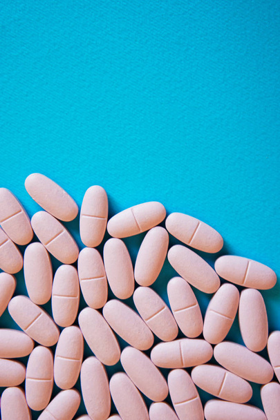Rózsaszín tabletták az alján a kék háttér. Egészségügy és az orvostudomány. Függőleges kép                            - Fotó, kép