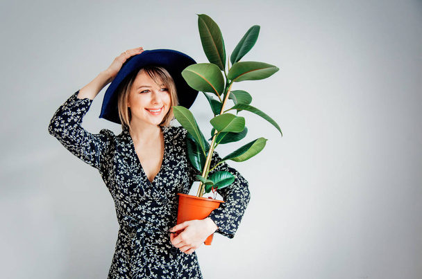 Mooie vrouw in trendy jurk met plant in een pot - Foto, afbeelding