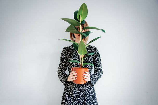Beautiful woman in trendy dress with plant in a pot - Фото, изображение