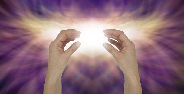 Senden transzendentaler Heilungsenergie - weibliche Hände einander gegenüber mit einem strahlend weißen Lichtstrahl dazwischen vor einem golden schimmernden Licht und rosa lila Energiehintergrund  - Foto, Bild