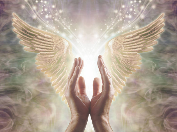 Het meten van engelachtige energie-mannelijke handen reiken tot een prachtig paar Gouden Engel vleugels met wit licht en schittert tussen, tegen een warme etherische energie vorming achtergrond - Foto, afbeelding