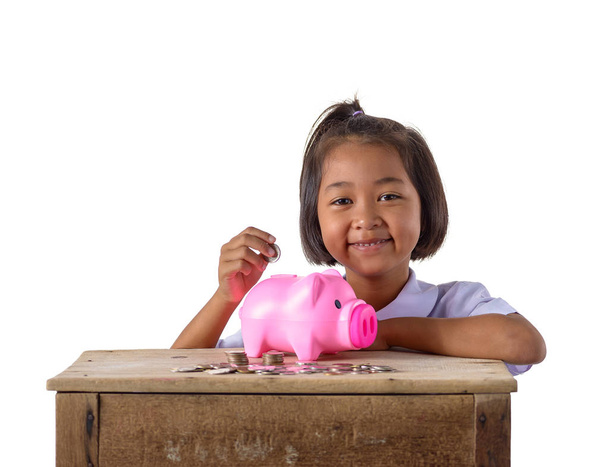 クリッピング パスと白い背景で隔離の貯金にコインを入れ制服かわいいアジアの女の子。教育貯蓄の概念 - 写真・画像
