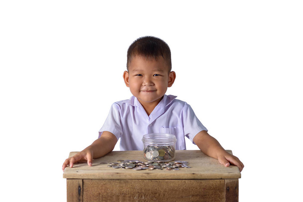 Mignon garçon de campagne asiatique en uniforme scolaire s'amuser avec des pièces dans un bol en verre isolé sur fond blanc avec chemin de coupe. Concepts d'épargne-études
 - Photo, image