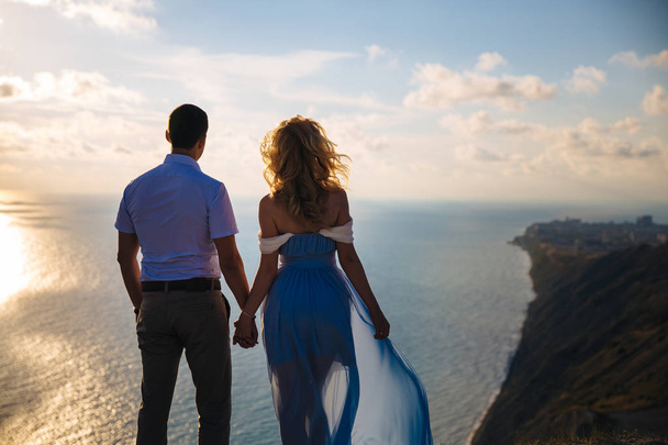 Silhouette eines liebenden Paares bei Sonnenuntergang. Mann umarmt eine Frau auf einem hohen Berg mit Blick auf das Meer. Konzept Familie, Liebe, Hochzeit, Flitterwochen. - Foto, Bild