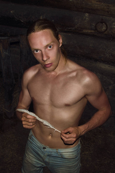 раздетый до пояса молодой человек в деревенском сарае с пером в руках
 - Фото, изображение