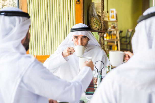 Group of middle eastern men wearing kandora bonding in a cafe' restarant in Dubai - 写真・画像