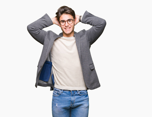Młody biznes człowiek noszenie okularów na na białym tle relaksująca i rozciąganie z ramiona i ręce za głowę z szyją, uśmiechający się zadowolony - Zdjęcie, obraz