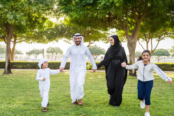 Happy middle-eastern family having fun in a park in Dubai - Parents and kids celebrating the weekend in the nature - Foto, Bild