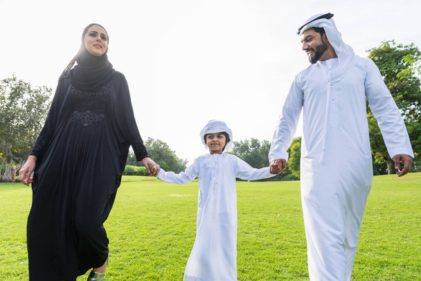 Happy middle-eastern family having fun in a park in Dubai - Parents and kids celebrating the weekend in the nature - 写真・画像