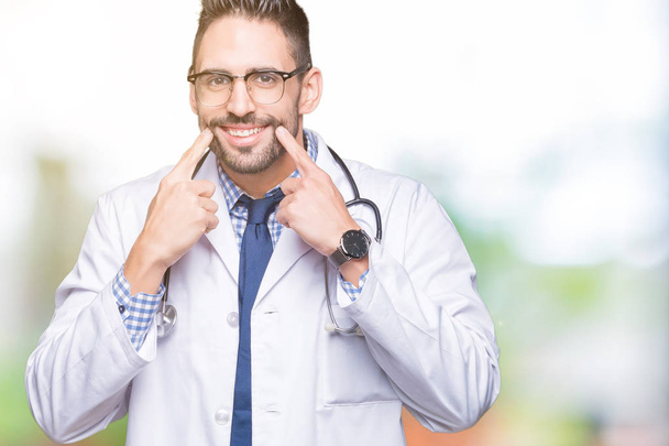Knappe jonge dokter man over geïsoleerd background Smiling met open mond, vingers wijzen en dwingen vrolijke glimlach - Foto, afbeelding