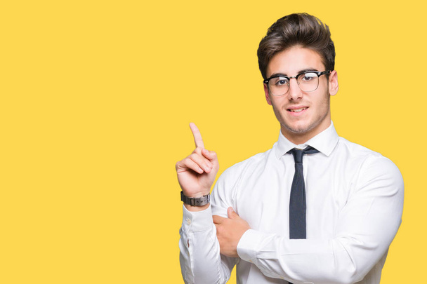 Young business man wearing glasses over isolated background with a big smile on face, pointing with hand and finger to the side looking at the camera. - Photo, Image