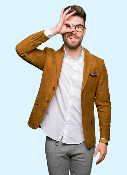 Jovem homem de negócios bonito usando óculos fazendo gesto ok com a mão sorrindo, olho olhando através dos dedos com o rosto feliz
. - Foto, Imagem
