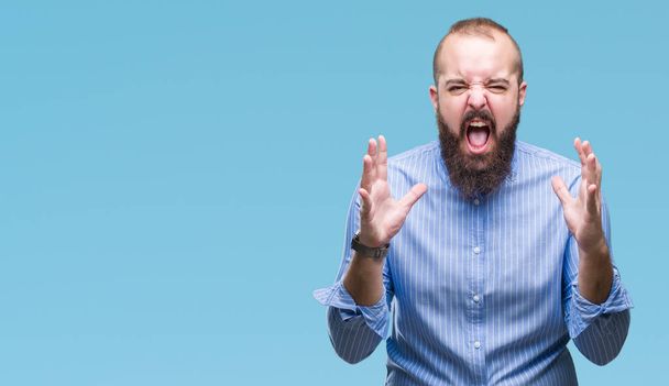 Young caucasian hipster man over isolated background crazy and mad shouting and yelling with aggressive expression and arms raised. Frustration concept. - Photo, Image