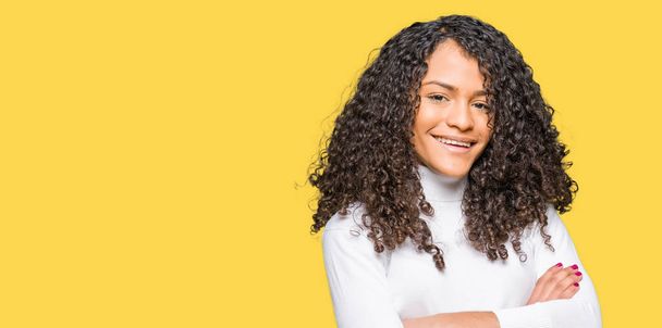 Young beautiful woman with curly hair wearing turtleneck sweater happy face smiling with crossed arms looking at the camera. Positive person. - Foto, imagen
