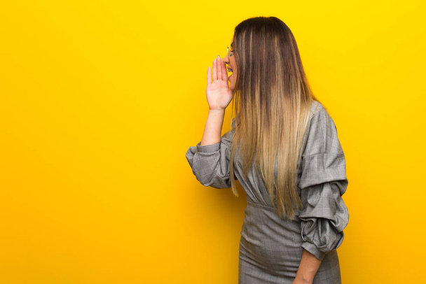 Νεαρή γυναίκα με τα γυαλιά πάνω από κίτρινο τοίχο φωνάζοντας με στόμα ορθάνοιχτο για την πλευρική - Φωτογραφία, εικόνα