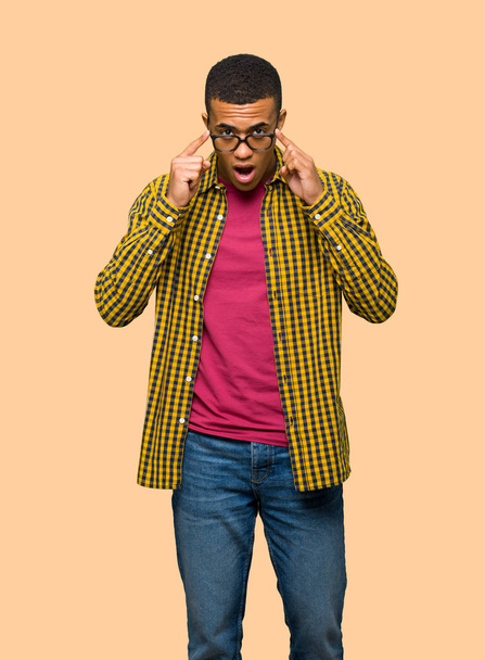 Young afro american man with glasses and surprised on isolated background - Foto, Imagem