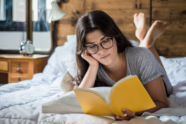 Young woman reading book on bed. concepts of home and comfort. - Foto, imagen