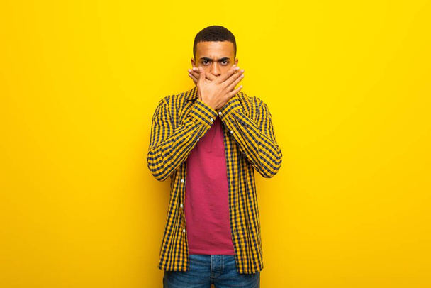 Jeune homme afro-américain sur fond jaune couvrant la bouche avec les mains pour avoir dit quelque chose d'inapproprié
 - Photo, image