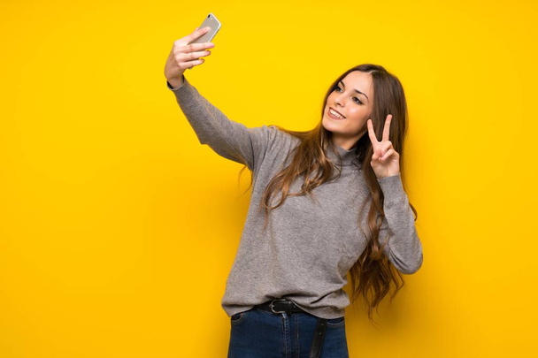 Молодая женщина за желтой стеной счастлива и указывает мобильный
 - Фото, изображение