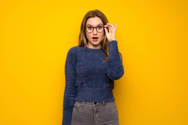 Dospívající dívka přes žlutou zeď s brýlemi a překvapený - Fotografie, Obrázek