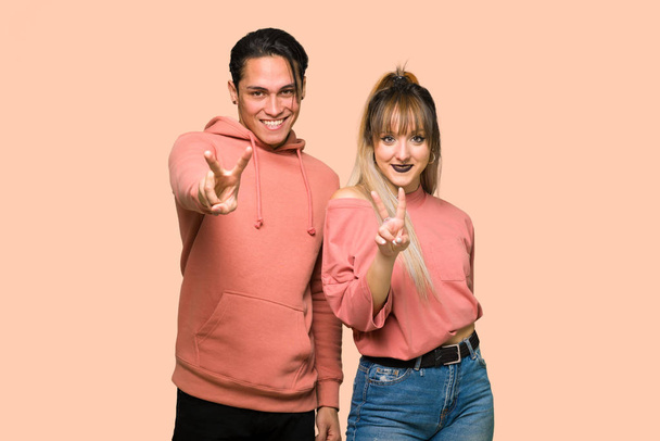 Mladý pár se usmívá a zobrazuje vítězné znaménko na růžovém pozadí - Fotografie, Obrázek
