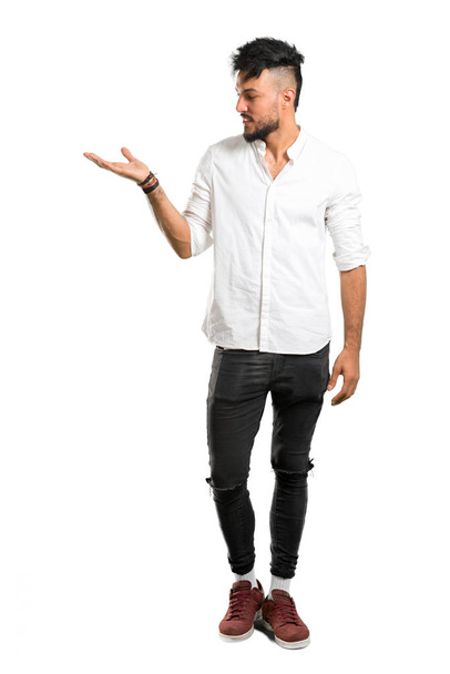 A full-length shot of a Arabic young man with white shirt holding copyspace imaginary on the palm on isolated white background - Photo, image