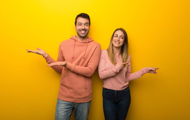 Group of two people on yellow background holding copyspace imaginary on the palm to insert an ad - Photo, Image