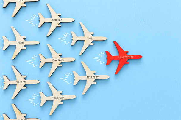 Leadership concept with airplanes on blue wooden background. One red leader flays ahead others. - Photo, image