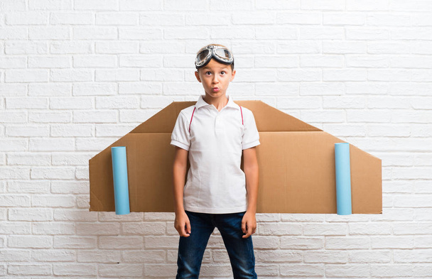 Boy playing with cardboard airplane wings on his back makes funny and crazy face emotion - 写真・画像