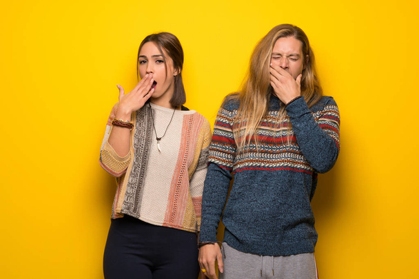 Couple hippie sur fond jaune bâillant et couvrant la bouche grande ouverte avec la main
 - Photo, image