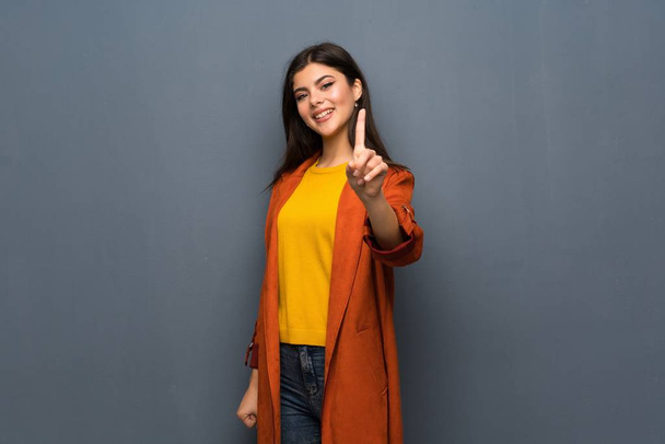 Teenager girl with coat over grey wall showing and lifting a finger - Foto, Imagem