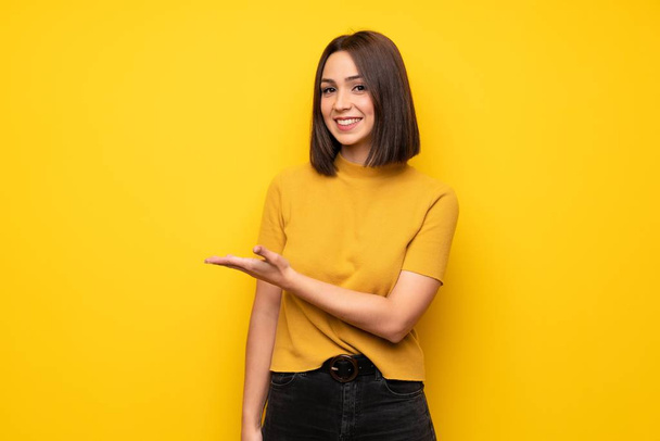 Jeune femme sur le mur jaune présentant une idée tout en regardant souriant vers
 - Photo, image