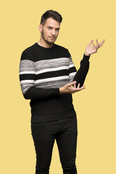 Handsome man extending hands to the side for inviting to come over yellow background - Photo, Image