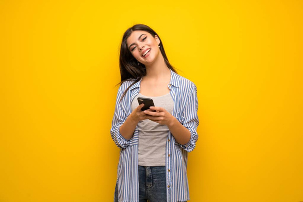 Teenagermädchen über gelbe Wand und sendet eine Nachricht mit dem Handy - Foto, Bild