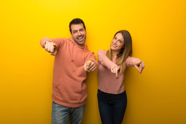 Sárga alapon két embercsoport mutat ujját, miközben mosolyogva - Fotó, kép