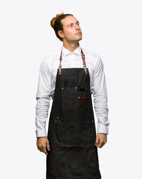 Homem barbeiro em um avental olhando para cima com cara séria em fundo isolado
 - Foto, Imagem