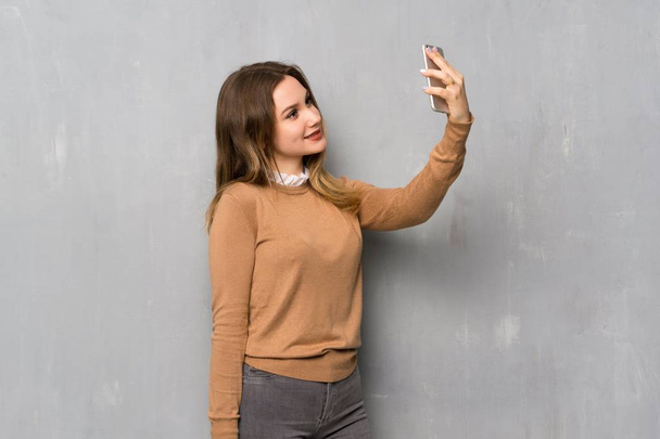 Tiener meisje over getextureerde muur maken een selfie - Foto, afbeelding