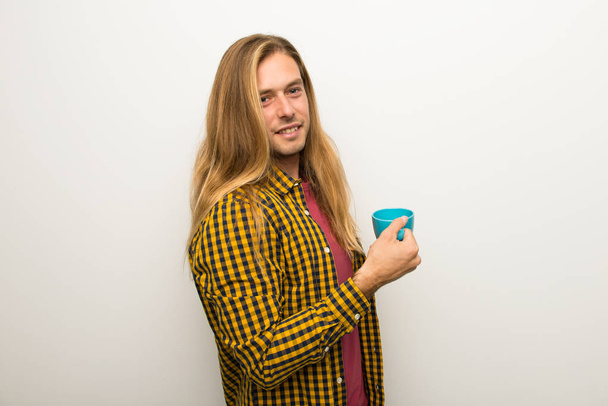 Blond man with long hair and with checkered shirt holding a hot cup of coffee - Photo, Image