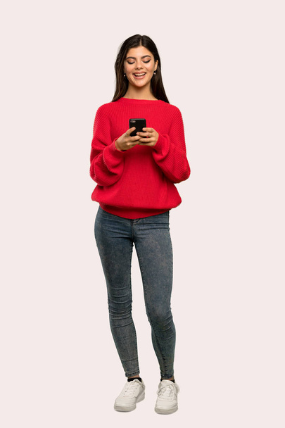 Полнометражный снимок девочки-подростка в красном свитере, отправляющей сообщение с мобильного на изолированном фоне
 - Фото, изображение