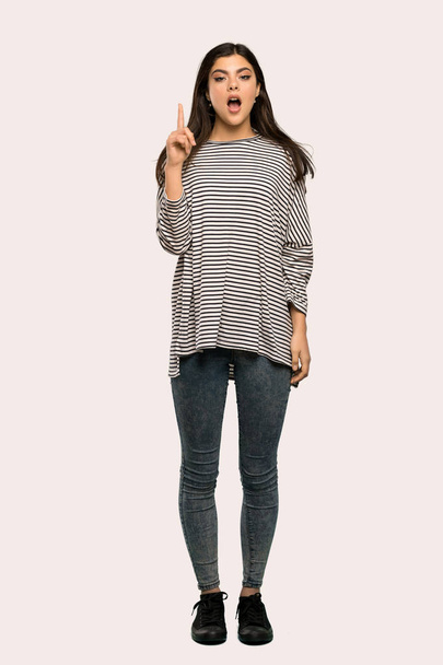 Un plano completo de una adolescente con camisa a rayas pensando en una idea apuntando con el dedo hacia arriba sobre un fondo aislado
 - Foto, Imagen