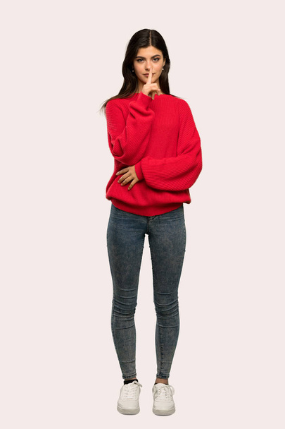 孤立した背景に口の中に指を入れて沈黙ジェスチャの記号を示す赤いセーターとティーンエイ ジャーの女の子のフルレングス ショット - 写真・画像
